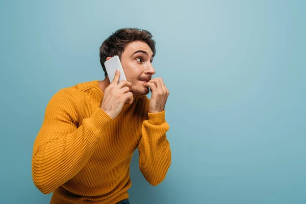 Handsome stressed man talking on smartphone, isolated on blue — Stock Photo