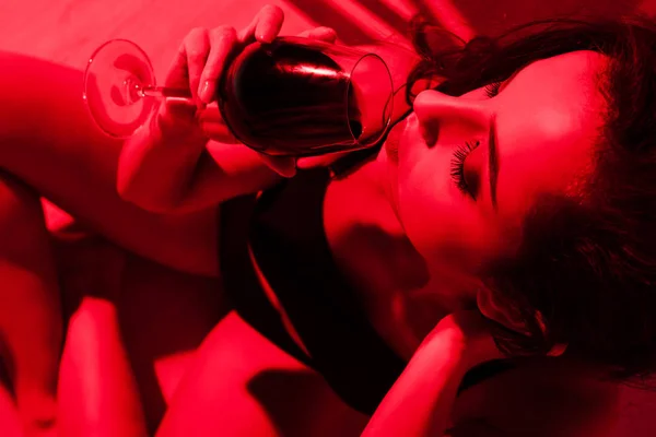 Beautiful sensual girl with glass of wine sitting in kitchen in red light — Stock Photo