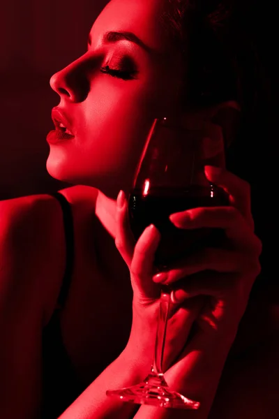 Hermosa chica sensual con copa de vino sentado en la luz roja - foto de stock