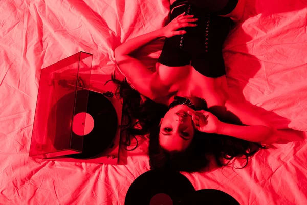 Attractive passionate woman lying on bed with vinyl records in red light — Stock Photo