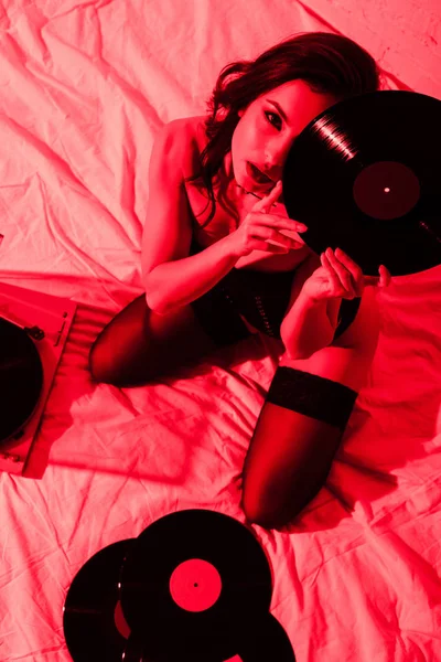 Beautiful passionate woman sitting on bed with vinyl records in red light — Stock Photo