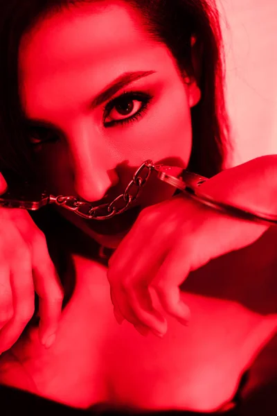 Beautiful seductive girl holding handcuff on red — Stock Photo