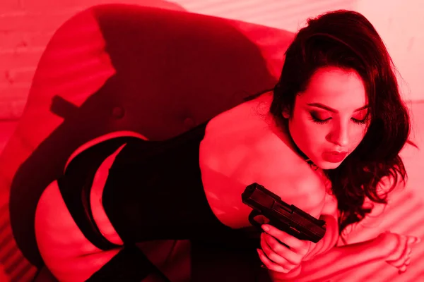 Пристрасна кримінальна жінка в боді-костюмі тримає пістолет на червоному — стокове фото