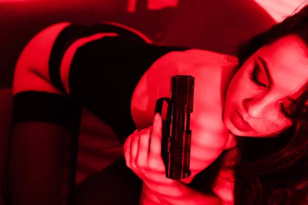 Attractive criminal sexy girl in bodysuit holding gun on red — Stock Photo