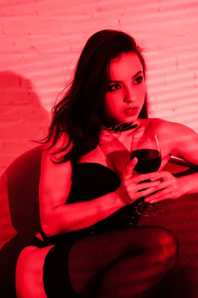 Sensuale donna seduta in poltrona con bicchiere di vino a luce rossa — Foto stock