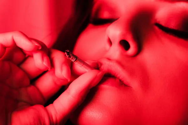 Attractive sexy woman smoking cigarette in red light — Stock Photo