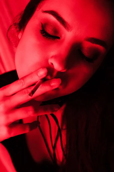 Beautiful sexy girl smoking cigarette in red light — Stock Photo