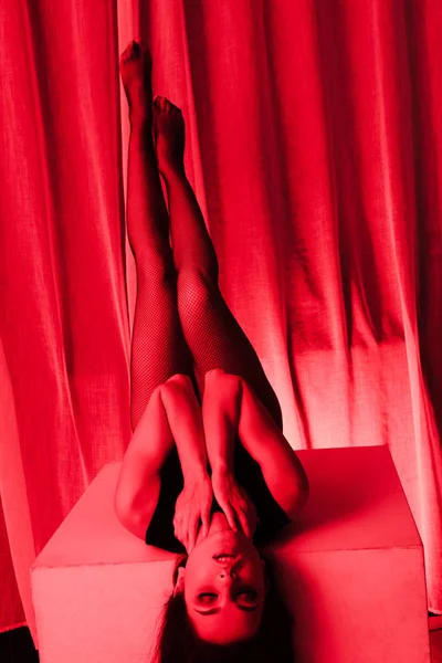 Attraktive sexy Frau posiert im Body und Netzstrumpfhose im Rotlicht — Stockfoto