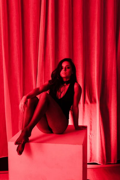 Mujer sensual posando en body y medias de rejilla en luz roja - foto de stock