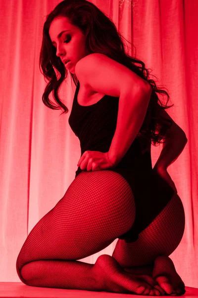 Seducente ragazza in posa in body e calze a rete a luce rossa — Foto stock