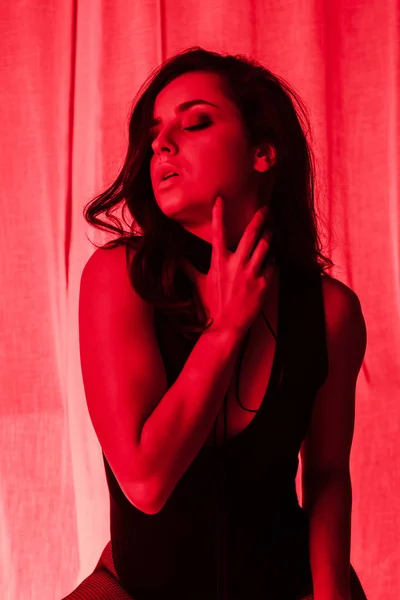 Beautiful seductive girl posing in bodysuit in red light — Stock Photo