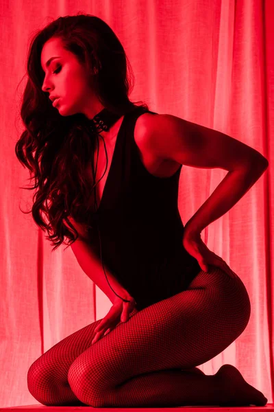 Leidenschaftliche junge Frau posiert im Body und Netzstrumpfhose im Rotlicht — Stockfoto