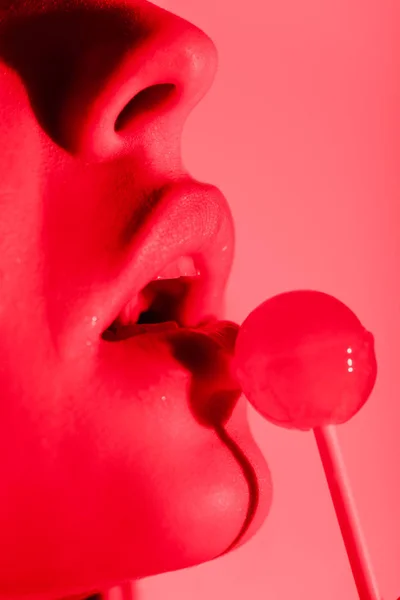 Cropped view of sexy girl eating lollipop in red light — Stock Photo