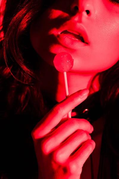 Vista recortada de mujer apasionada atractiva comer piruleta en la luz roja - foto de stock