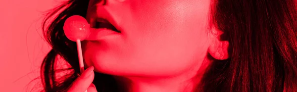Обрезанный вид сексуальной девушки едят леденец в красном свете, панорамный снимок — стоковое фото