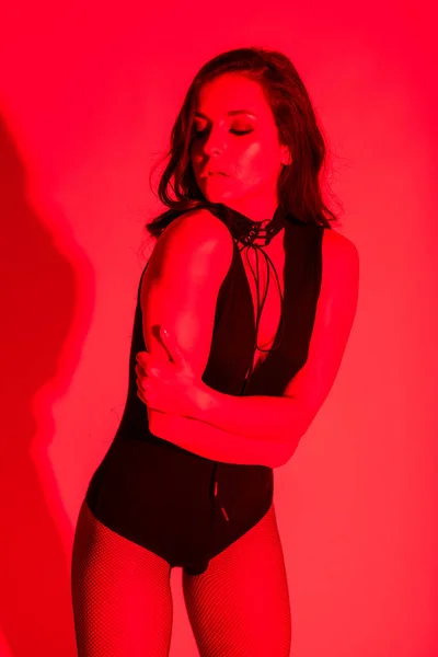 Beautiful sexy young woman posing in bodysuit, isolated on red — Stock Photo