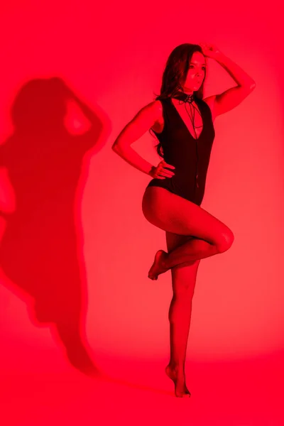 Hermosa mujer joven apasionada posando en maillot negro, aislado en rojo - foto de stock