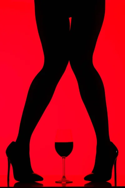 Vista ritagliata di silhouette nera di donna sexy con bicchiere di vino isolato su rosso — Foto stock