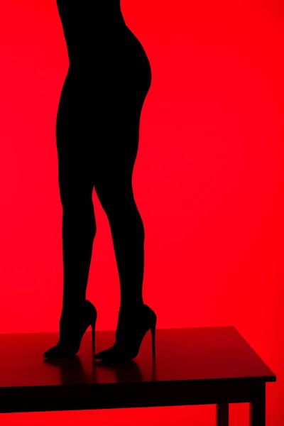 Schwarze Silhouette einer sexy eleganten Frau in High Heels, die auf einem Tisch posiert, isoliert auf Rot — Stockfoto