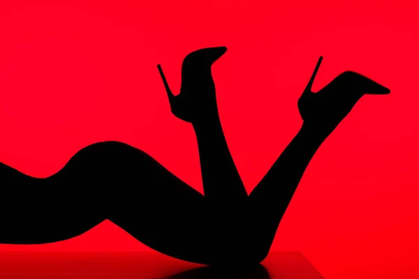 Silueta negra de mujer sensual en tacones posando sobre mesa aislada sobre rojo - foto de stock