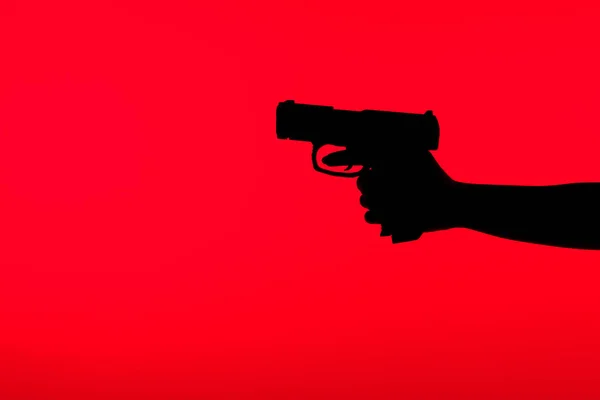 Cropped view of silhouette of criminal woman holding gun in hand isolated on red — Stock Photo