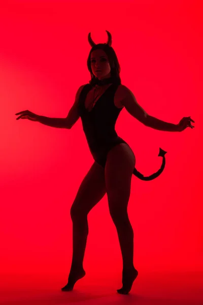 Силуэт соблазнительной девушки, позирующей в костюме Дьявола, изолированной на красном — стоковое фото