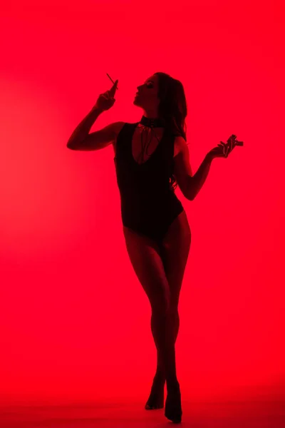 Silueta de chica sexy sosteniendo encendedor fumar cigarrillo aislado en rojo - foto de stock