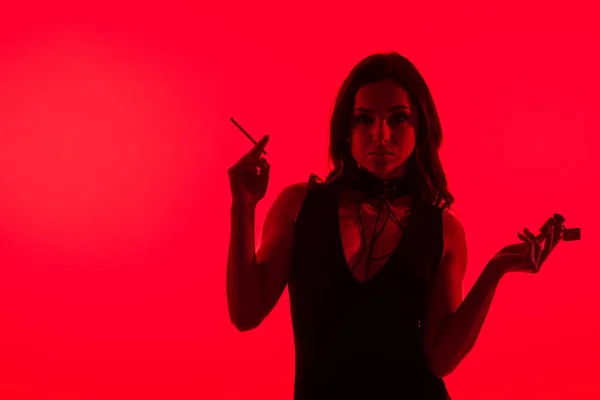 Silueta de hermosa chica sensual sosteniendo encendedor fumar cigarrillo aislado en rojo - foto de stock