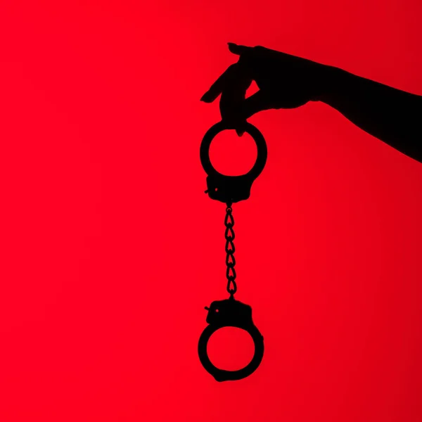 Cropped view of silhouette of sexy girl holding handcuff, isolated on red — Stock Photo