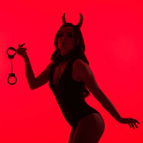Силует пристрасної жінки в костюмі Диявола, що тримає наручники, ізольовані на червоному — стокове фото