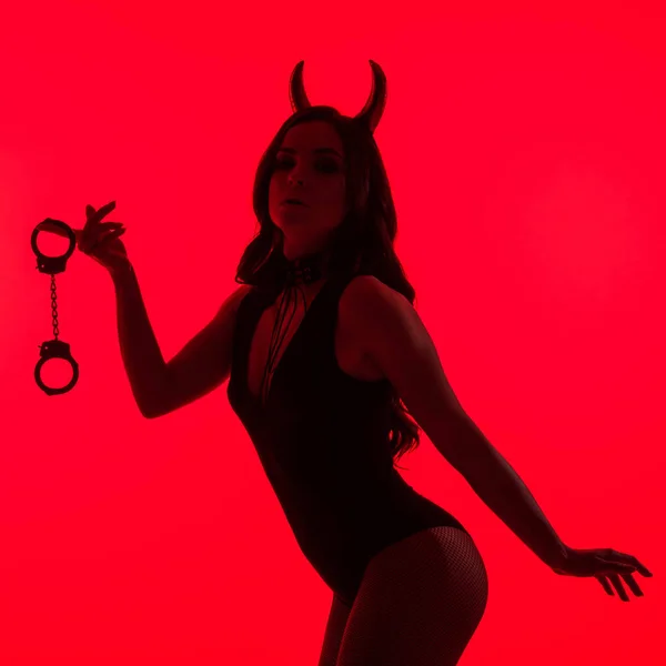 Silhueta de mulher apaixonada em traje Diabo segurando algemas, isolado em vermelho — Fotografia de Stock