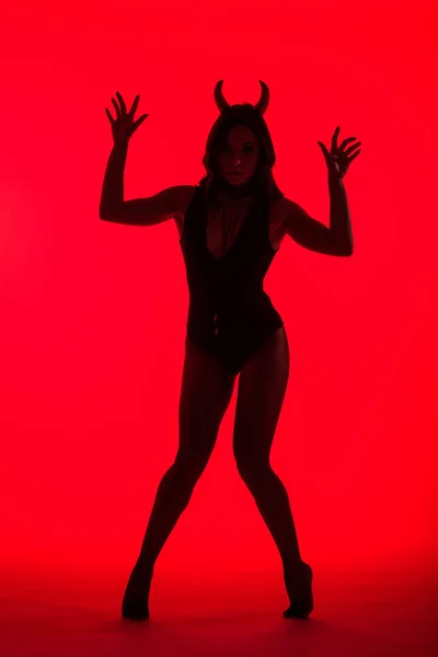 Silhouette of beautiful young woman in Devil costume, isolated on red — Stock Photo