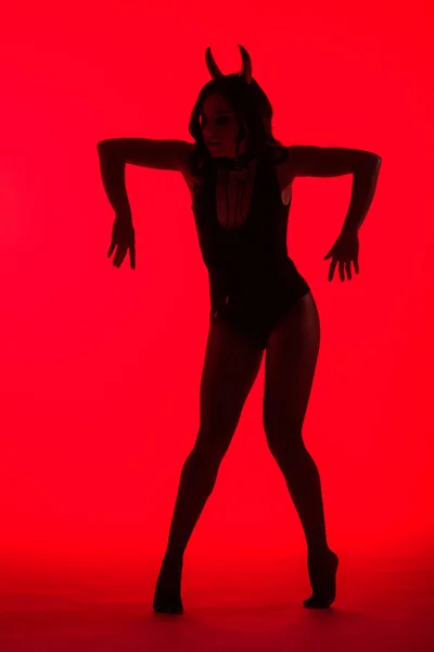 Силуэт сексуальной молодой женщины в костюме Дьявола, изолированный на красном — стоковое фото