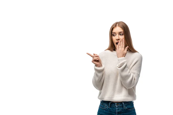 Shocked young woman in white sweater pointing and covering mouth, isolated on white — Stock Photo