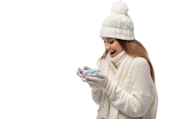 Femme excitée en écharpe, gants et chapeau regardant boîte cadeau, isolé sur blanc — Photo de stock