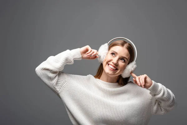 Bella ragazza felice posa in maglione bianco e scalda orecchie, isolato su grigio — Foto stock