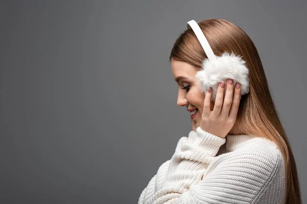 Porträt eines lächelnden Mädchens, das in weißem Pullover und Ohrenschützer posiert, isoliert auf grau — Stockfoto