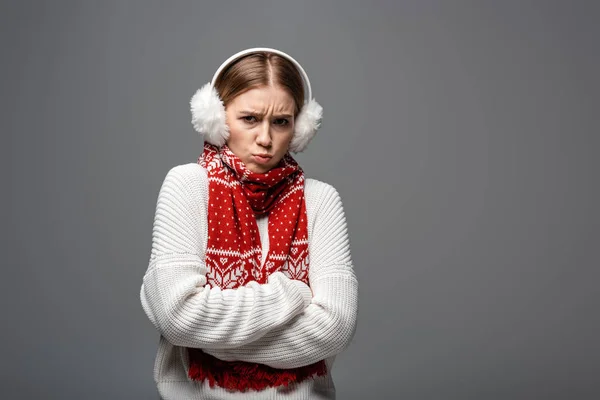 Offeso fredda ragazza in maglione bianco, paraorecchie e sciarpa posa con le braccia incrociate, isolato su grigio — Foto stock
