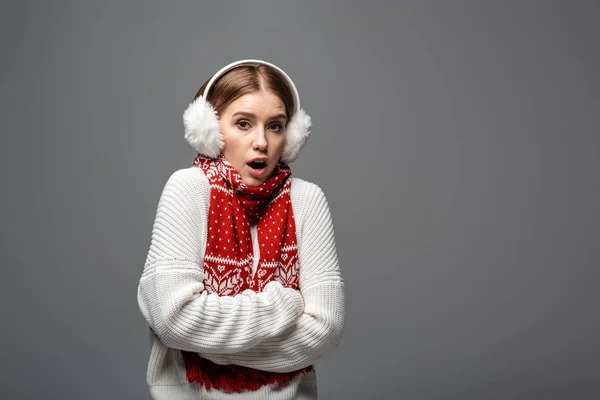Attractive shocked girl in white sweater, earmuffs and scarf posing with crossed arms, isolated on grey — Stock Photo