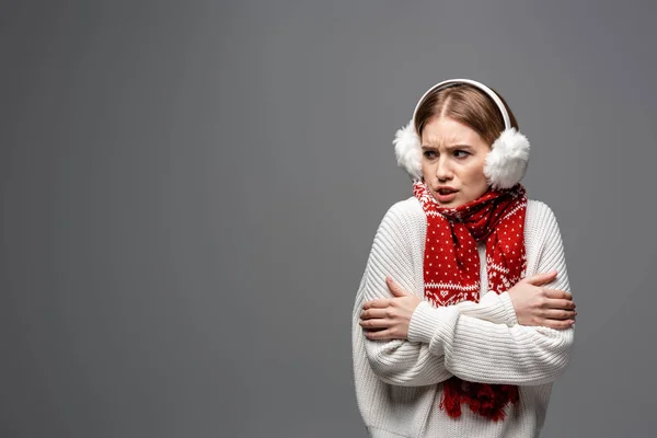 Cold angry girl in white sweater, earmuffs and scarf posing with crossed arms, isolated on grey — Stock Photo