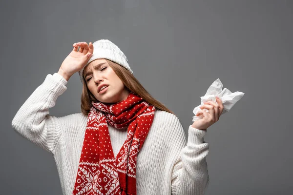 Femme malade épuisée en bonnet tricoté ayant mal à la tête et tenant une serviette en papier, isolée sur gris — Photo de stock