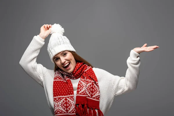 Attractive excited woman in knitted hat and scarf presenting something, isolated on grey — Stock Photo