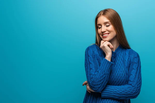 Привлекательная мечтательная женщина с закрытыми глазами в голубом трикотажном свитере, изолированная на голубом — стоковое фото