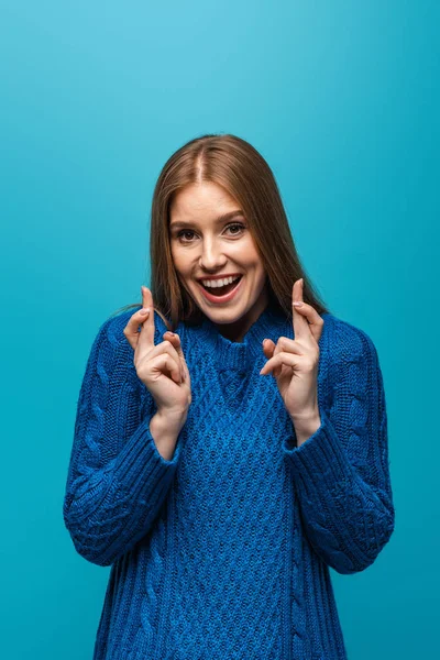 Красива жінка в синьому в'язаному светрі з схрещеними пальцями, ізольована на синьому — стокове фото