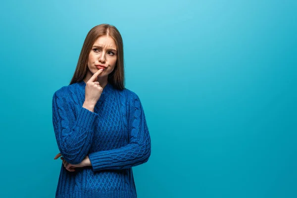 Beautiful pensive woman in blue knitted sweater, isolated on blue — Stock Photo