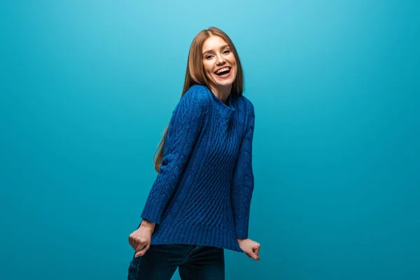 Atractiva mujer positiva en suéter de punto azul, aislado en azul - foto de stock