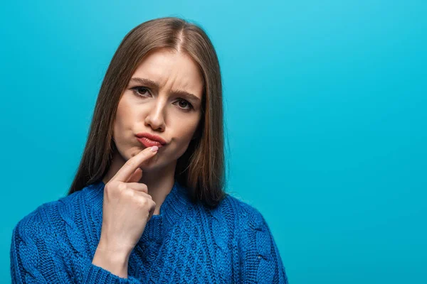 Atractiva mujer reflexiva en suéter de punto azul, aislado en azul - foto de stock