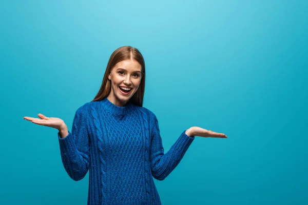 Femme excitée avec geste haussant les épaules en pull tricoté bleu, isolé sur bleu — Photo de stock
