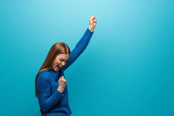 Beautiful cheerful woman in blue knitted sweater celebrating triumph, isolated on blue — Stock Photo
