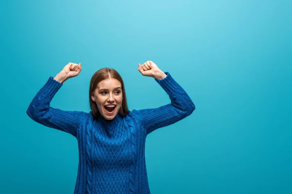 Attraktive, glückliche Frau in blauem Strickpullover, die Erfolge feiert, isoliert auf blau — Stockfoto